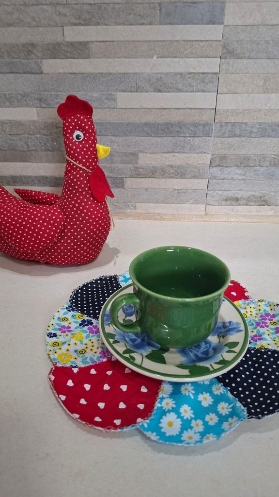 Galinha de tecido vermelha de bolinhas e porta-copo de retalhos coloridos com xícara verde