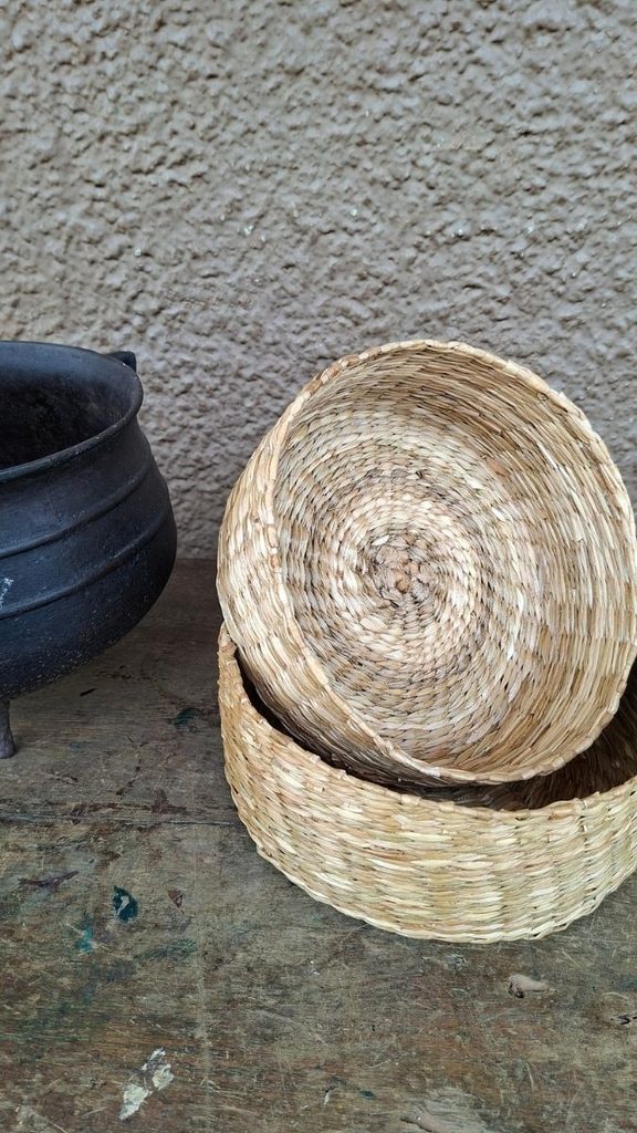 Dois cestos de fibra natural trançada em espiral ao lado de panela de ferro sobre mesa de madeira rústica