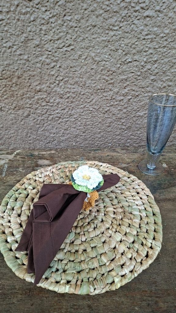 Fotografia de produto com celular: sousplat de fibra natural trançada com guardanapo e porta-guardanapo de crochê sobre mesa de madeira rústica e piso texturizado